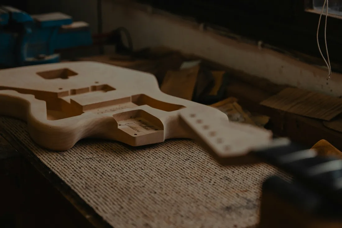 Cuerpo de guitarra sin acabar apoyado sobre el banco de un taller de lutería, con las cavidades ya vaciadas y virutas alrededor